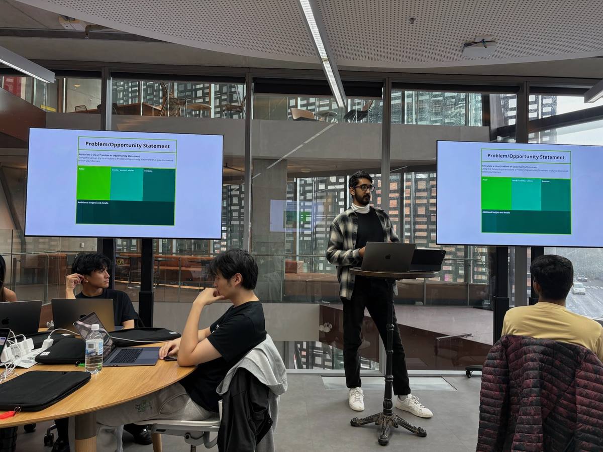 Noah facilitating the Problem/Opportunity Statement canvas, shown on two screens, in front of a cohort.