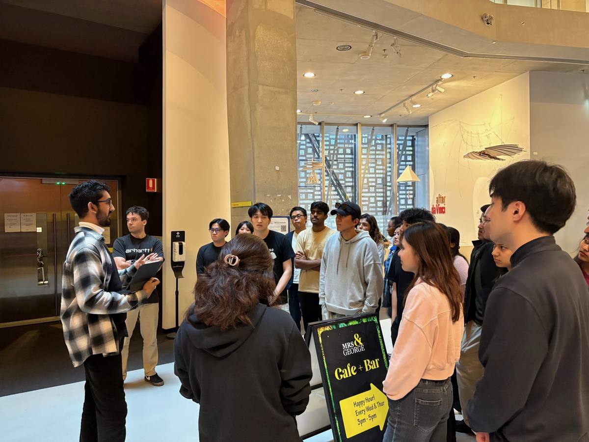 Noah leading a cohort on a walkthrough, holding an iPad, with the group gathered around him.