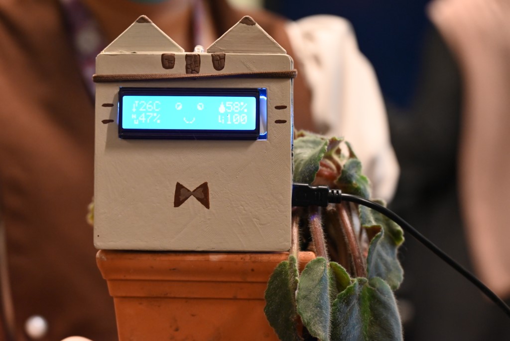 The Sprout Cat prototype: a cat-eared box on a terracotta plant pot, its LCD screen showing live plant readings and a smiling face