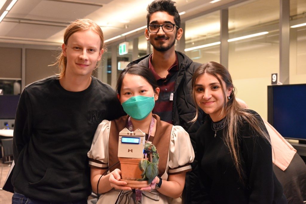 Four of the five-person project team at the UTS Tech Festival, holding the SproutCat prototype in its pot plant