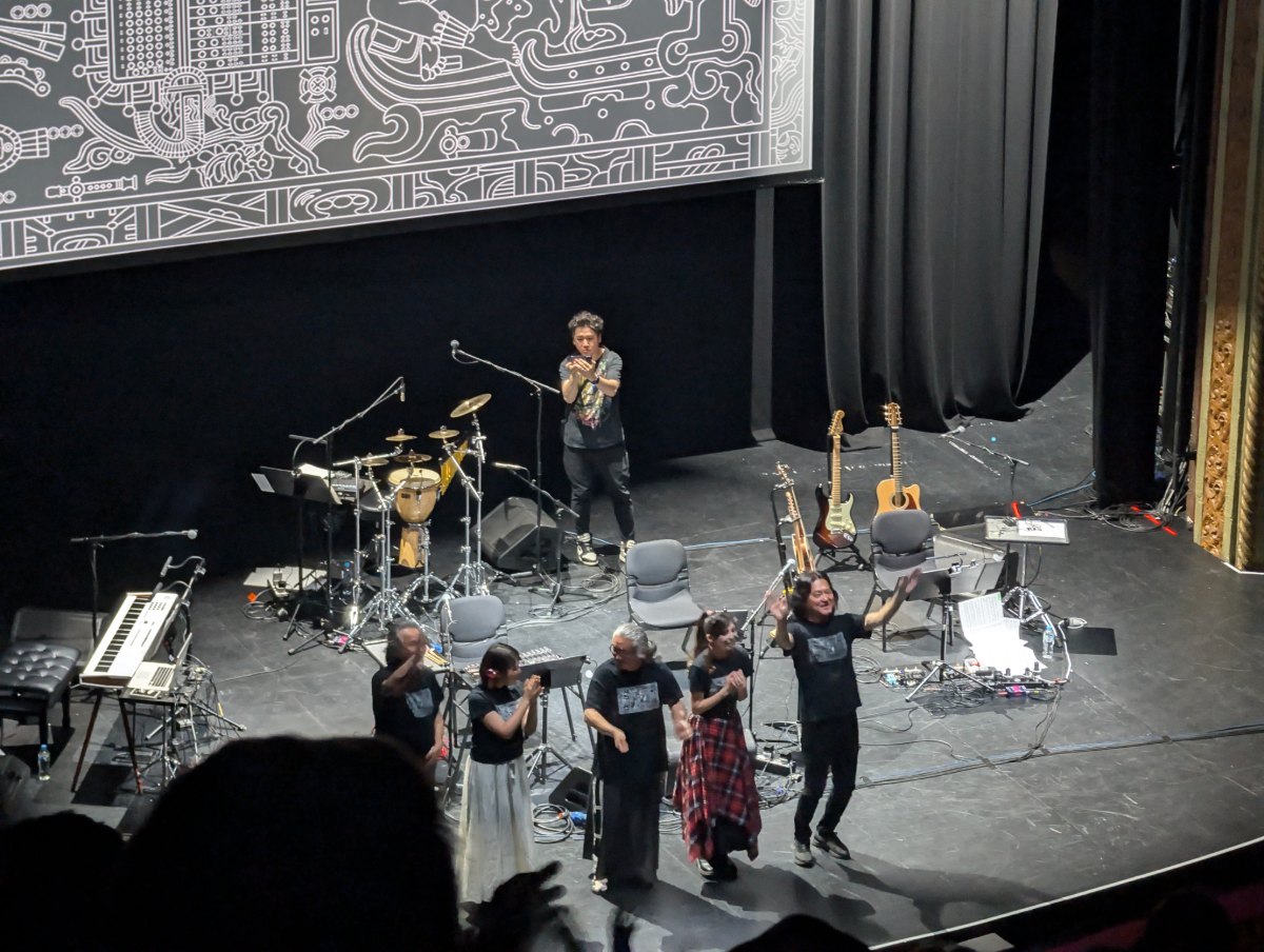 Musicians taking a bow on stage at a Final Fantasy concert, with guitars, a keyboard and a drum kit behind them