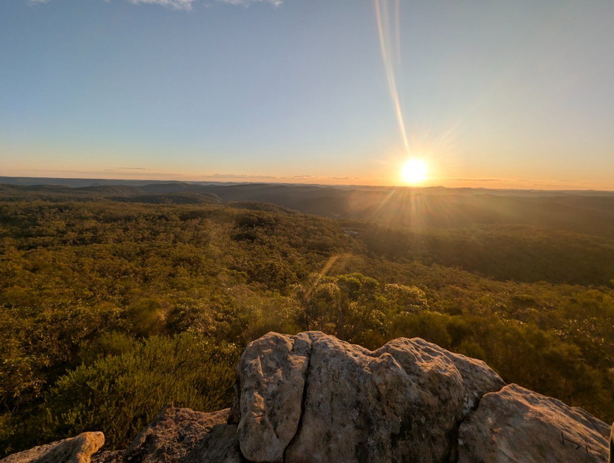 Sun low over a bushland valley, seen from a sandstone lookout