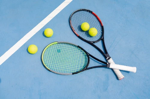 Two tennis rackets and four tennis balls on a blue court