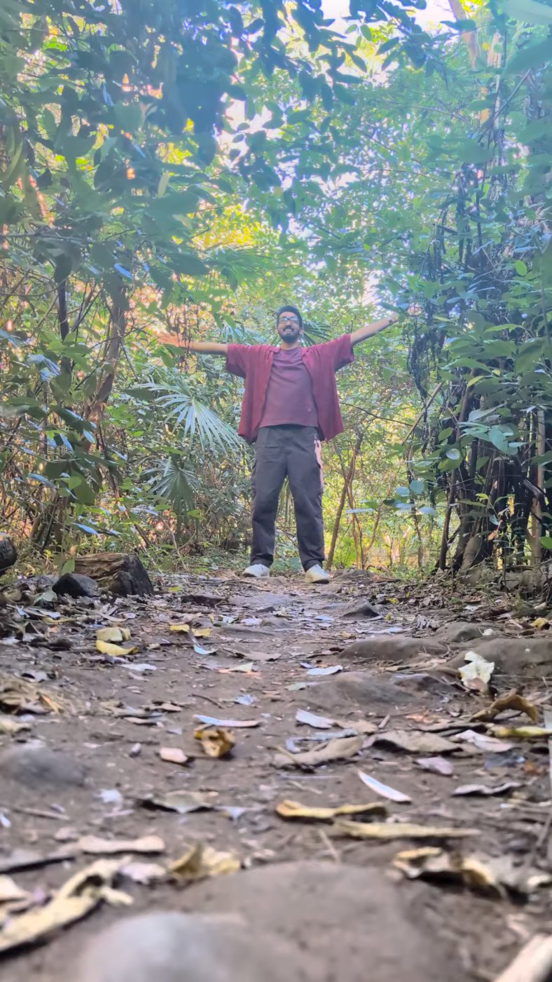Noah Koshy standing on a forest track with both arms spread wide, seen from ground level